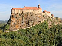 Das Foto zeigt den gepflasterten Weg hinauf zur Burg Riegersburg. Im Hintergrund erkennen wir einige SchülerInnen die sich zur Riegersburg auf den Weg machen und die Riegersburg selbst